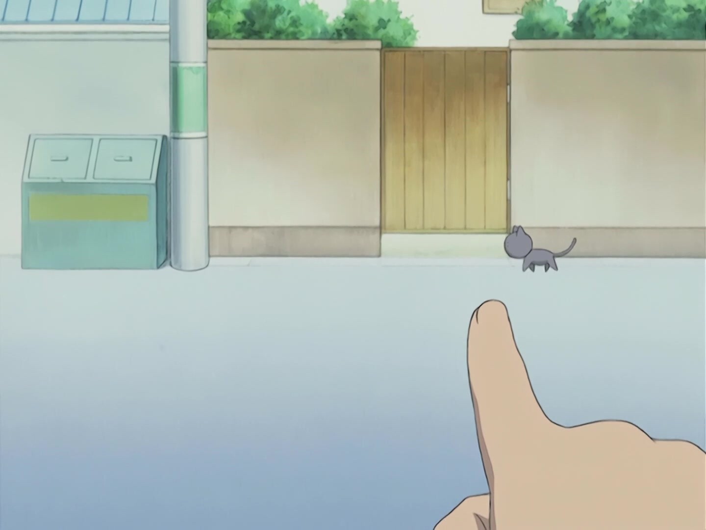 A screenshot from Azumanga Daioh. The biting cat is walking outside, and there is a finger in frame pointing at the cat.